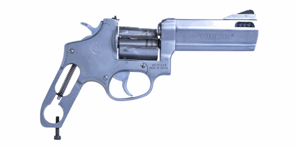 Revolver s vytrženým bočním krytem rámu a odkrytým mechanismem, s viditelnými pružinami; poškození po havárii zbraně